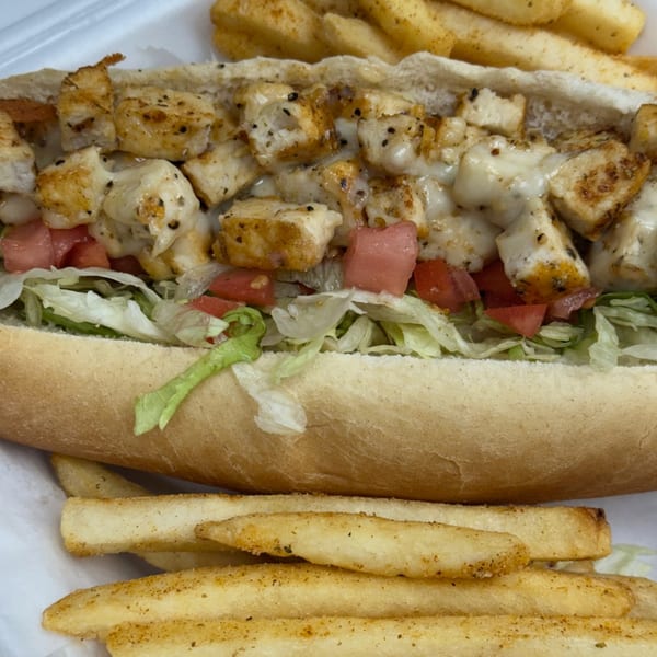 A chicken cheesesteak sandwich with lettuce and tomatoes, served with a side of fries.