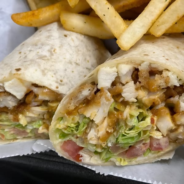 Two halves of a chicken wrap with lettuce, tomato, and sauce, served with french fries.