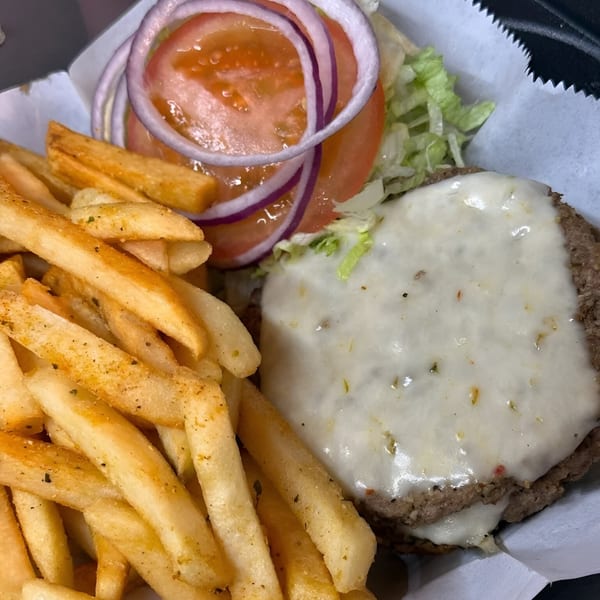 A cheeseburger with lettuce, tomato, and red onion, served with a side of seasoned fries.
