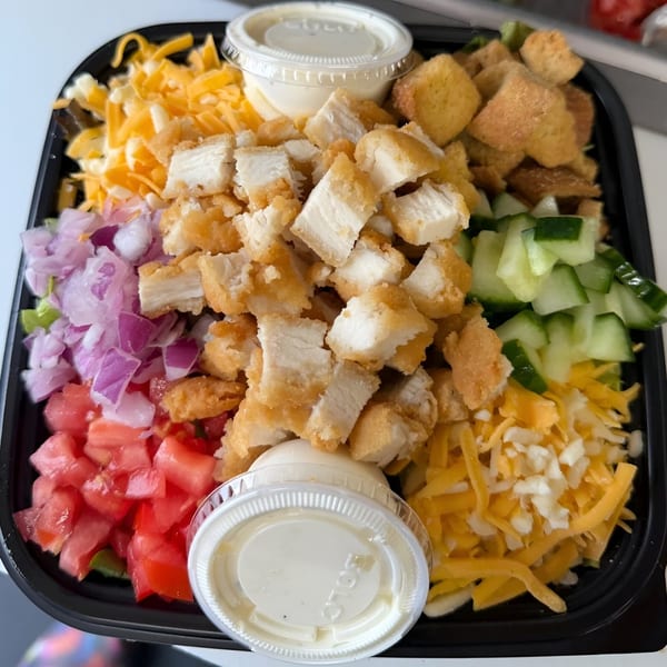 A Sweet Suite 216 salad with crispy chicken, cheese, tomatoes, onions, cucumbers, and croutons.